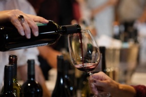 Mão serve vinho tinto em uma taça durante uma degustação.